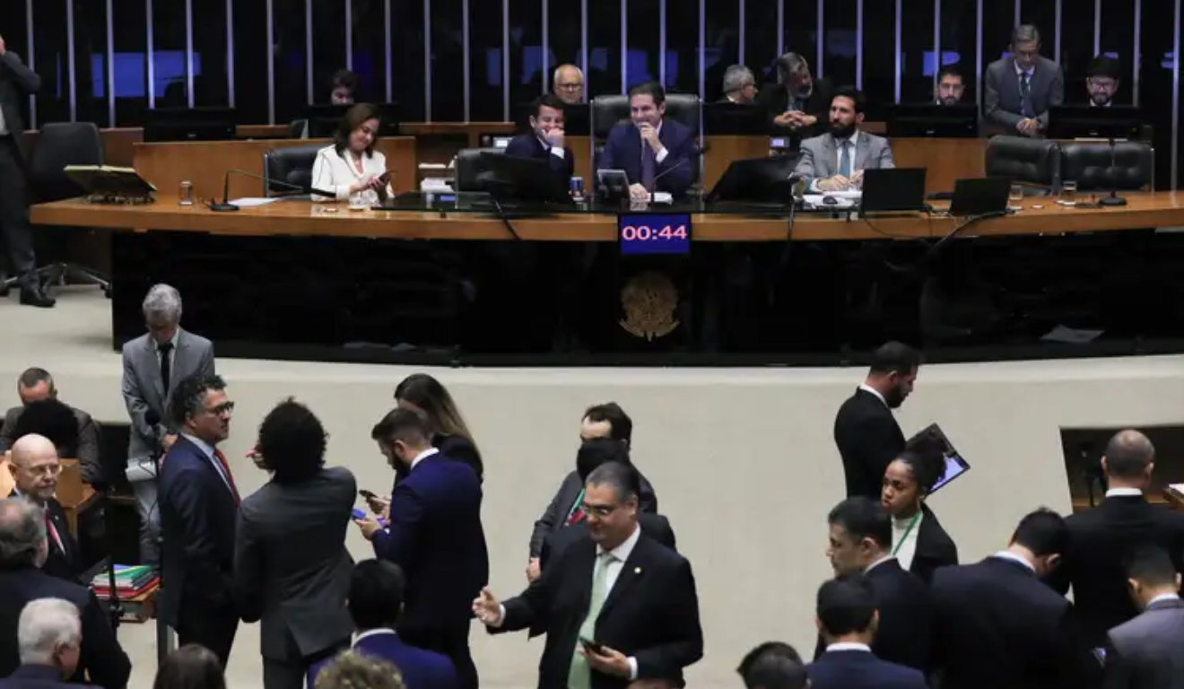 Câmara dos Deputados aprovou a urgência do PL que determina a isenção do IR para quem ganha até R$ 5 mil. Na imagem, vemos um plano aberto da Câmara durante uma sessão, com parlamentares conversando.