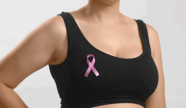 Entenda tudo sobre o câncer de mama. Na imagem, vemos o busto de uma mulher branca, que usa um top preto e o laço do outubro rosa no lado direito.