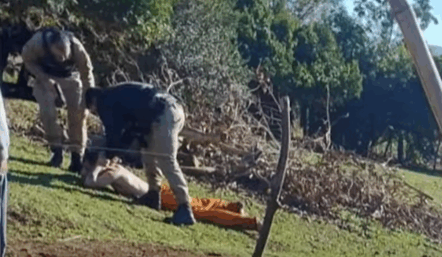 Dois policiais em uma área de mata prendendo um fugitivo.