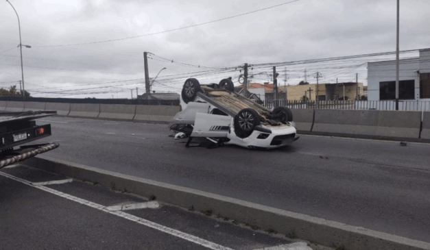 Carro branco capotado em rodovia.