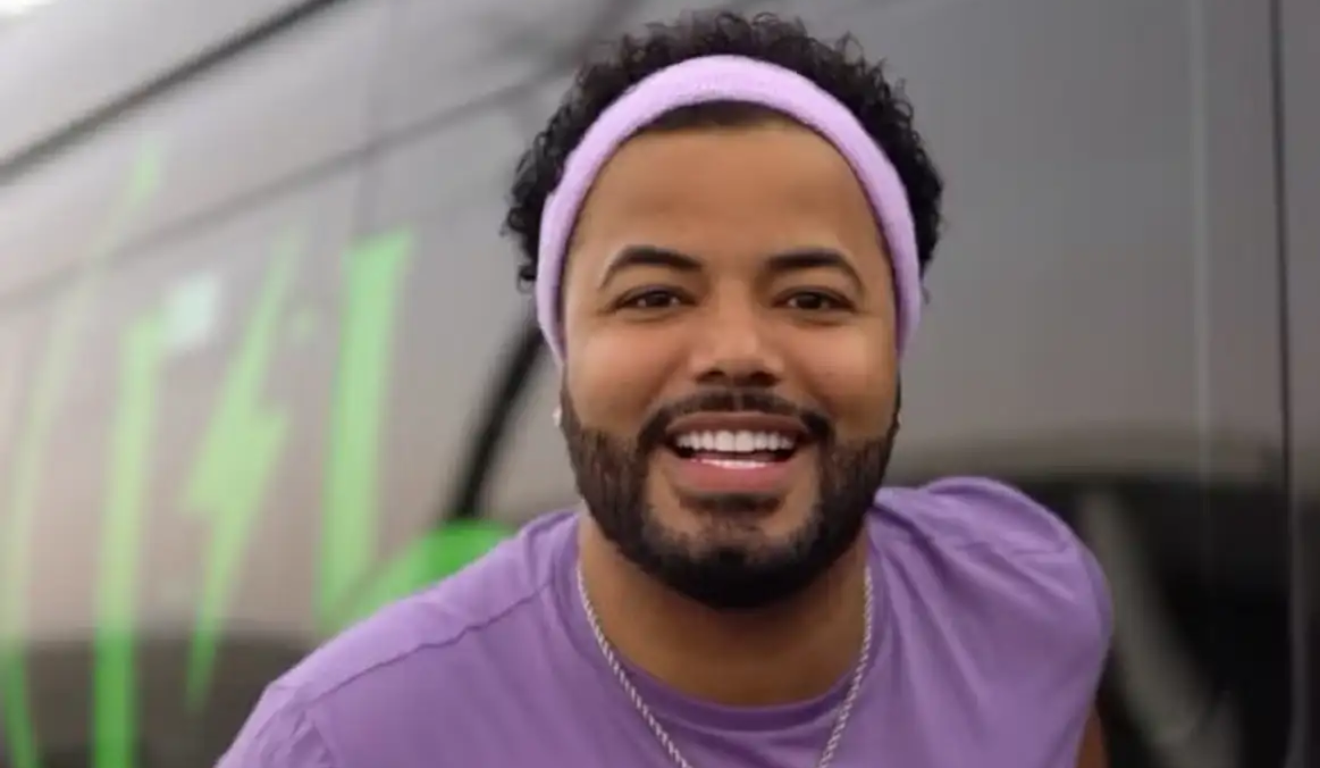 Hytalo Santos é transferido para presídio na Paraíba. Na imagem, vemos o influenciador sorrindo para a foto, utilizando uma camiseta roxa e uma faixa roxa no cabelo. Hytalo Santos é um homem negro de cabelo e barba pretos.