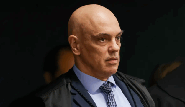 Na imagem, o ministro do STF Alexandre de Moraes, que disse que bancos podem ser punidos se aplicarem sanções americanas. Moraes é um homem branco e careca. Na foto, ele utiliza um blazer azul escuro, uma camisa azul clara e uma gravata azul escuro.