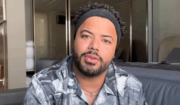 O Ministério Público do Trabalho da Paraíba pediu o bloqueio dos bens de Hytalo Santos. Na imagem, vemos o influenciador em foto posada. Ele é um homem negro, de barba e cabelos pretos. Hytalo usa uma faixa preta na cabeça e uma camisa cinza.