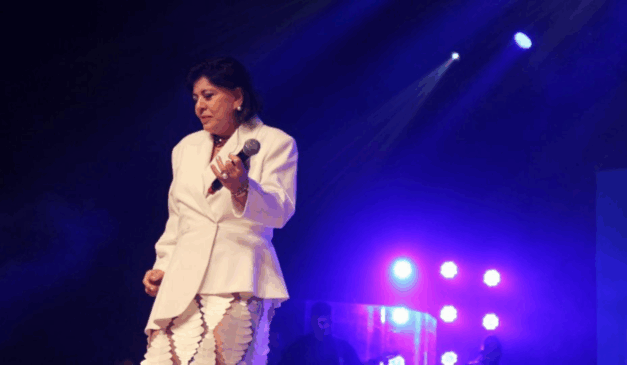 Cantora Roberta Miranda vestida de branco em apresentação, segurando o microfone na mão esquerda.