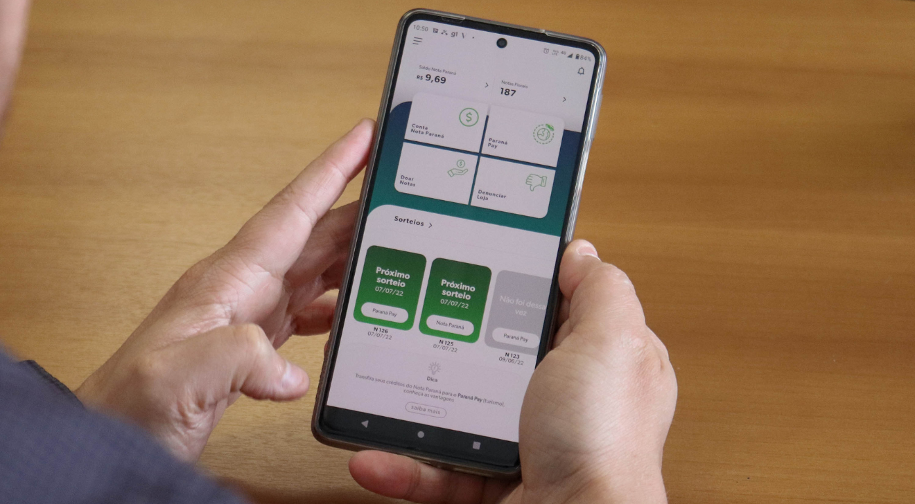 uma pessoa segura um celular. Na tela está a interface do aplicativo Nota Paraná.