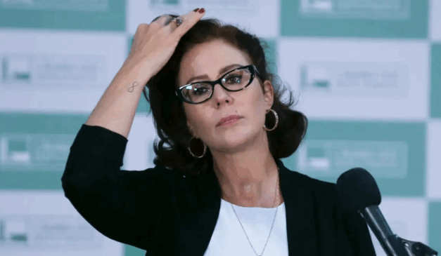 A Justiça italiana mantém a prisão da deputada Carla Zambelli por risco de fuga. Carla é uma mulher branca, de cabelo preto. Ela usa um óculos meia-lua com armação preta, além de um blazer preto e uma camiseta branca.