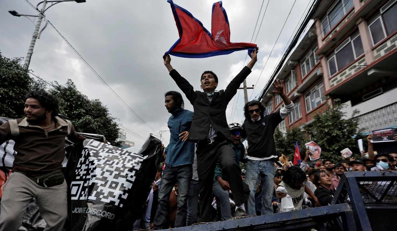 O Exército do Nepal começou a ocupar as ruas após um dia de protestos no país. Na imagem, vemos manifestantes. No centro, um deles está com a bandeira do país.