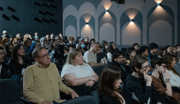 Imagem de pessoas sentadas assistindo algo dentro de uma sala de cinema.