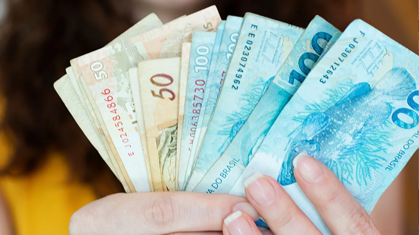 Descubra como ganhar na Lotomania com 0 acertos. Na imagem, vemos a mão de uma pessoa branca segurando notas de R$ 100 e R$ 50.