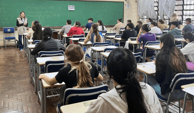 A Unioeste abriu as inscrições para o Vestibular 2026. Na imagem, vemos a sala de uma prova de vestibular, com alunos sentados em carteiras escolares realizando a prova.