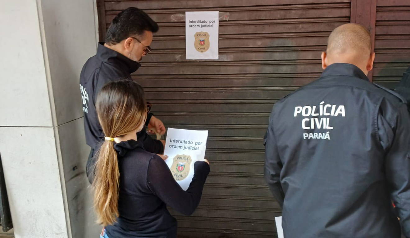 A Polícia Civil do Paraná fechou uma ótica que usava os dados de clientes para realizar empréstimos. Na imagem, vemos os agentes da polícia colocando um papel escrito "Interditado por ordem judicial" na fachada da loja.
