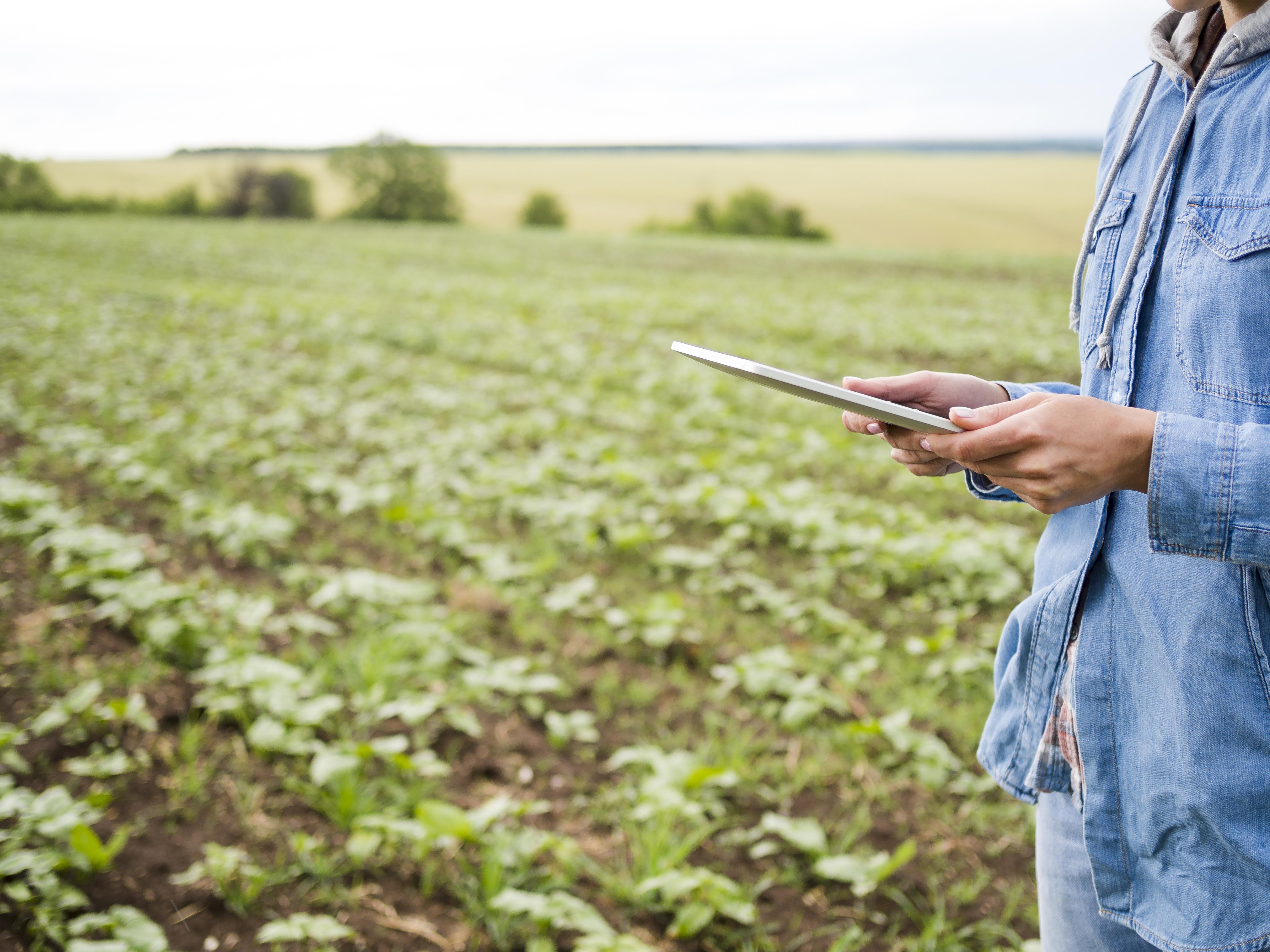 Produtor rural usando tablet em plantação, representando os agricultores afetados pela restrição geográfica ilegal da Resolução CMN 5247.