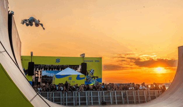 Foto da competição do Vert Battle, com um skatista fazendo manobra em uma rampa, com o sol se ponto ao fundo