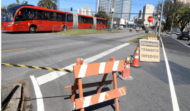 O Centro de Curitiba será bloqueado para obras do BRT Leste/Oeste. Na imagem, vemos uma placa em uma avenida de Curitiba informando que o trânsito está impedido, além de cones bloqueando o local.