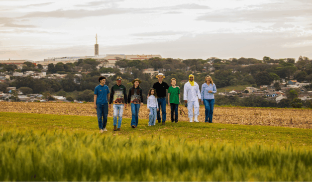 agricultores caminhando no campo e, ao fundo, a fábrica da Copacol