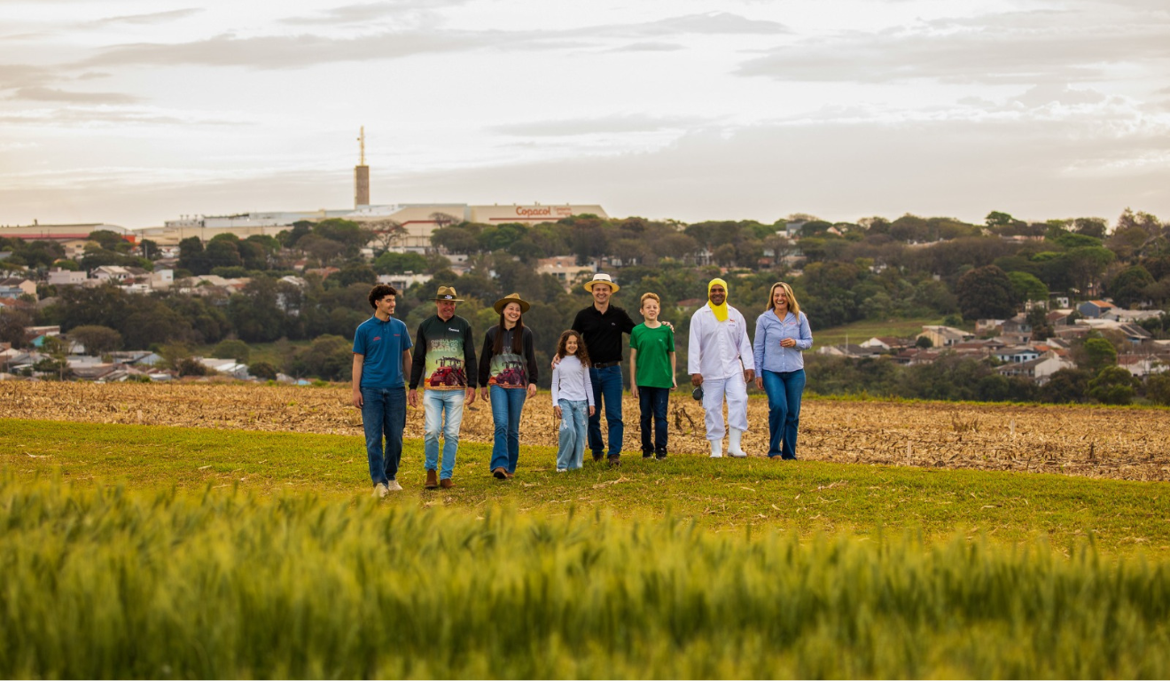 agricultores caminhando no campo e, ao fundo, a fábrica da Copacol