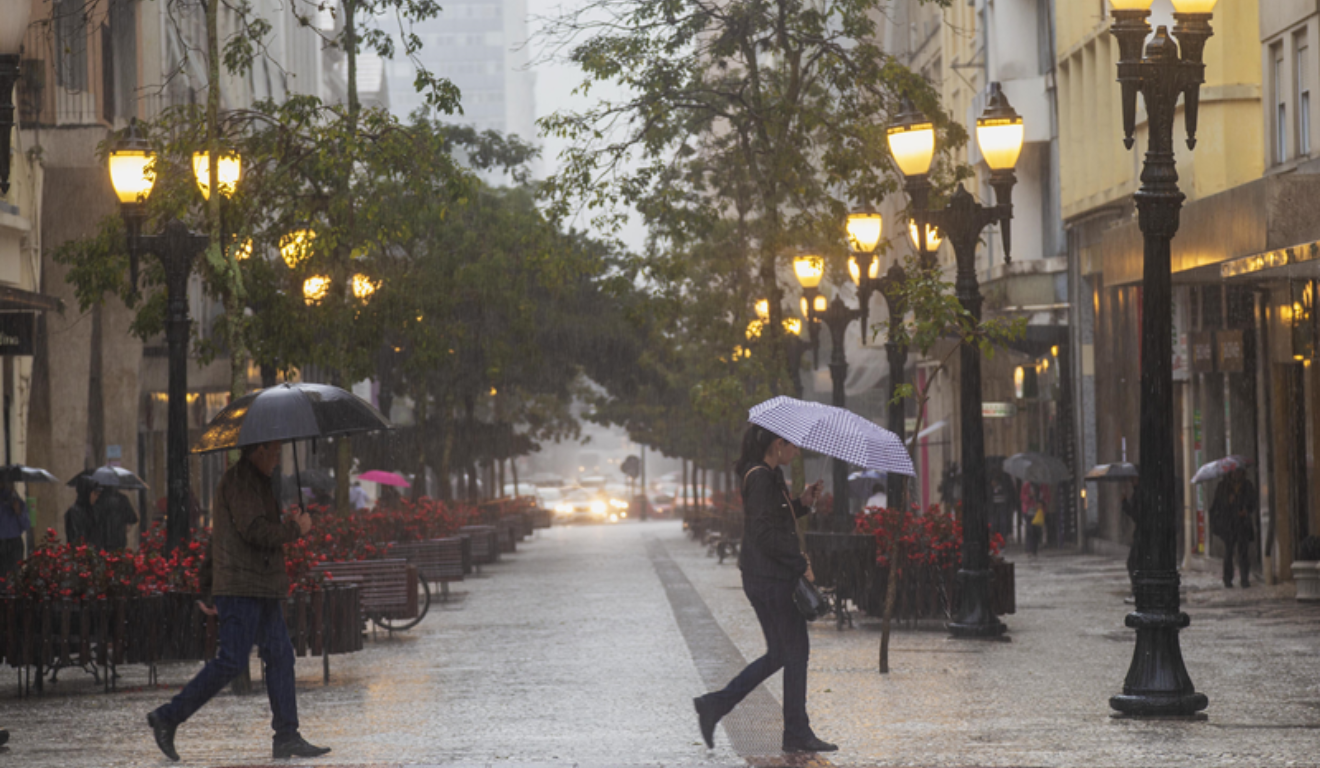 Curitiba registrou chuva em quase metade do ano. Na imagem, vemos a Rua das Flores, em Curitiba, durante um dia de chuva. Duas pessoas estão andando e segurando guarda-chuvas.