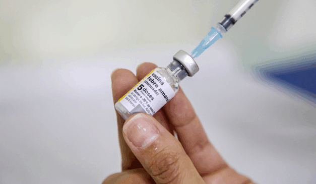 A partir deste sábado (11), Curitiba abre unidades de saúde para vacinação. Na imagem, vemos um vidro com um imunizante para febre amarela, enquanto uma agulha de vacina está extraindo o conteúdo.