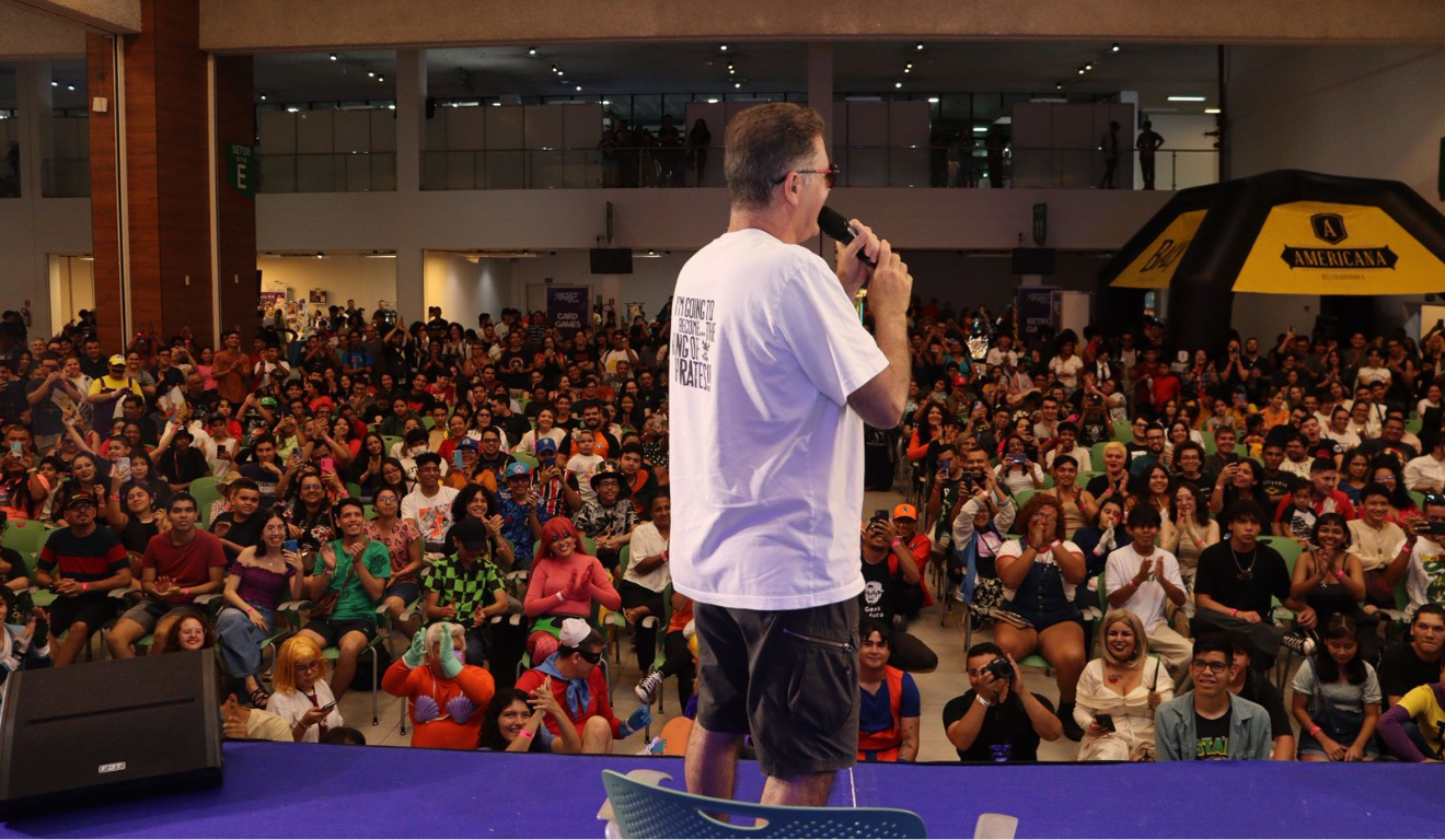 Em outubro, acontece o Shinobi Spirit, um festival de cultura pop em Curitiba. Na imagem, vemos um apresentador falando com o público do evento. Ele está de costas para a câmera, e vemos os visitantes, vários deles com fantasias de personagens famosos do universo geek.