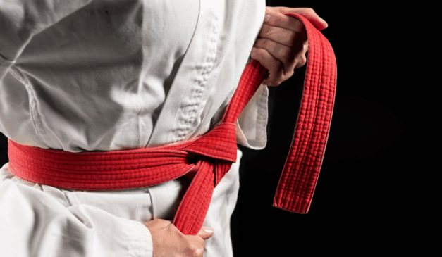 Uma garota utilizou golpes de jiu-jitsu para imobilizar o pai. Na imagem ilustrativa, vemos mãos femininas brancas amarrando a faixa vermelha de um kimono branco para artes marciais.