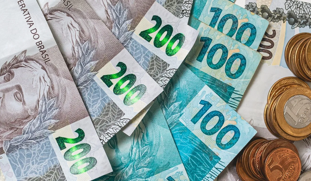 Saiba se o ganhador da Loteria Federal precisa pagar imposto. Na imagem, vemos notas de R$ 200, R$ 100 e uma moeda de R$ 1.