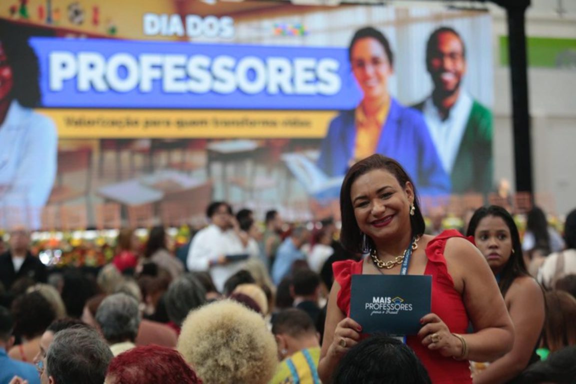 mulher vestida de vermelho segurando placa escrito mais professores