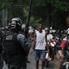 Policial segura arma enquanto moradores dos complexos de favelas do Alemão e da Penha protestam do lado de fora da sede do governo do Estado do Rio de Janeiro 29/10/2025