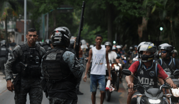 Policial segura arma enquanto moradores dos complexos de favelas do Alemão e da Penha protestam do lado de fora da sede do governo do Estado do Rio de Janeiro 29/10/2025