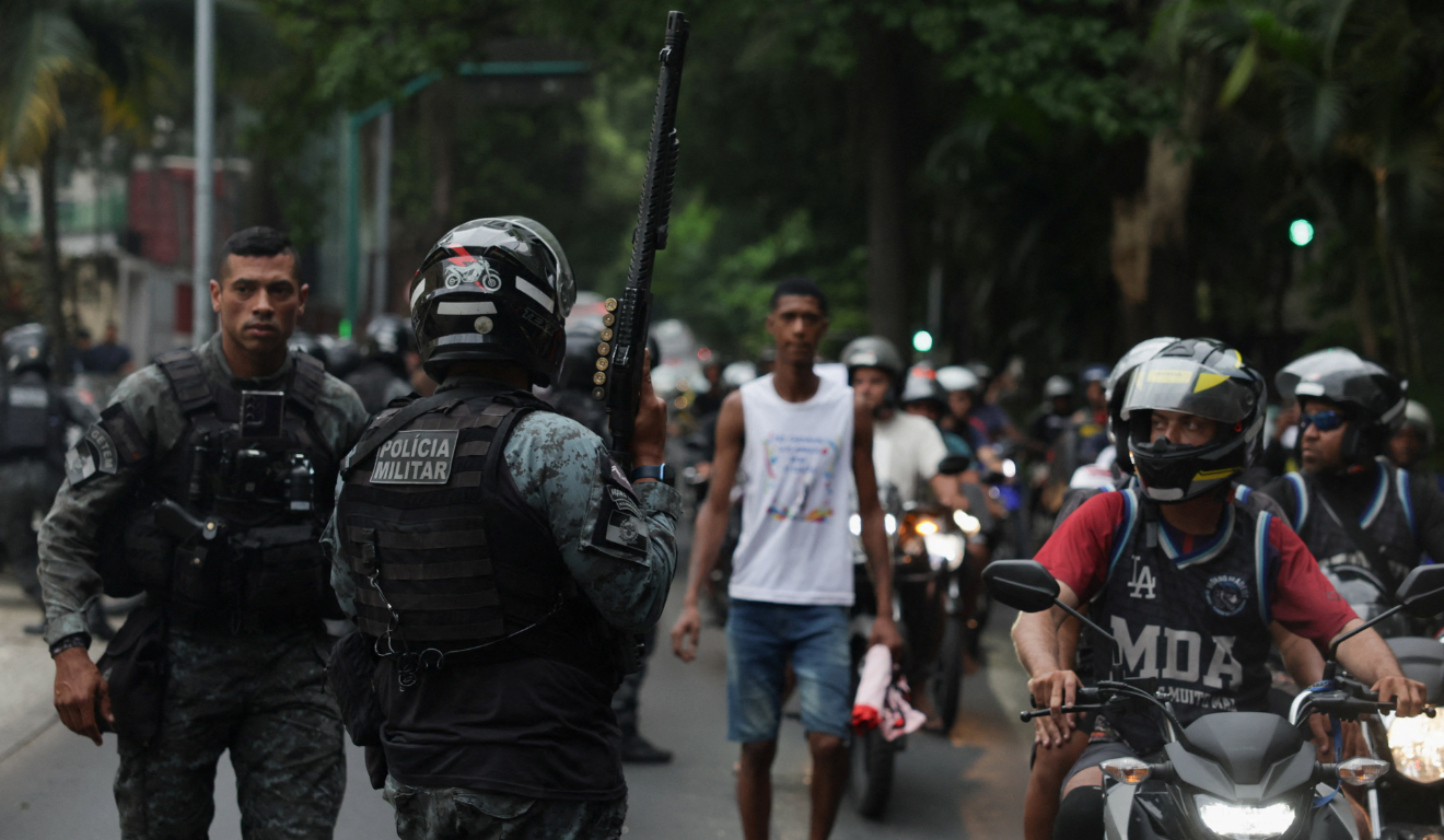 Policial segura arma enquanto moradores dos complexos de favelas do Alemão e da Penha protestam do lado de fora da sede do governo do Estado do Rio de Janeiro 29/10/2025