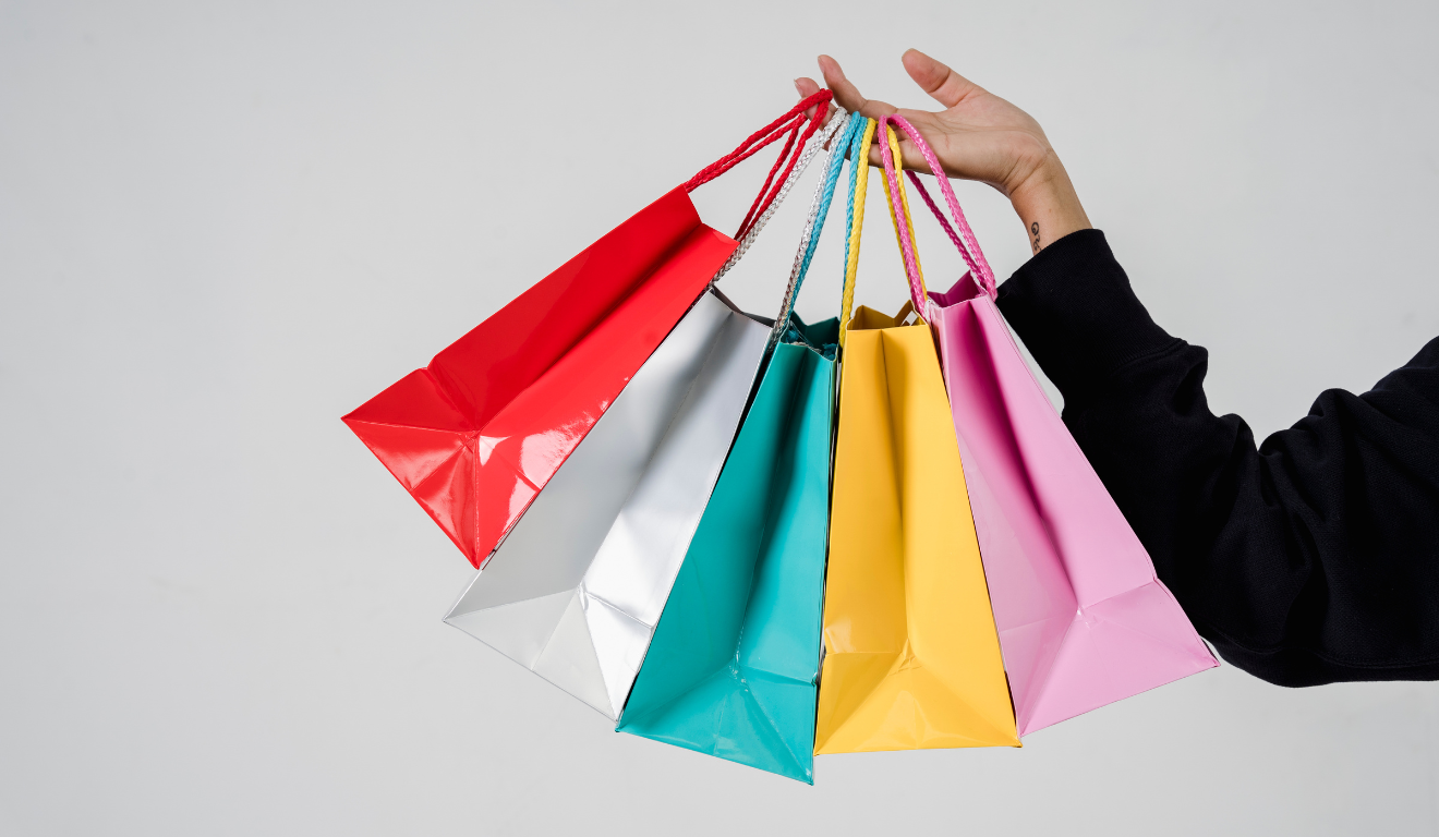 Conheça 5 estratégias para vender mais na Black Friday 2025. Na imagem ilustrativa, vemos uma mão de uma pessoa branca segurando diversas sacolas de compras.