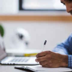 Imagem ilustrativa de homem escrevendo em caderno e na frente do computador, em alusão aos cursos gratuitos EAD do Senac Paraná