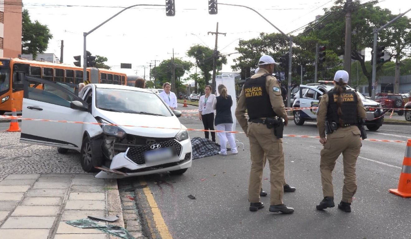 Local do acidente acompanhado por policiais militares, que observam carro de aplicativo, que mulher e filha estavam, antes de acidente com ônibus
