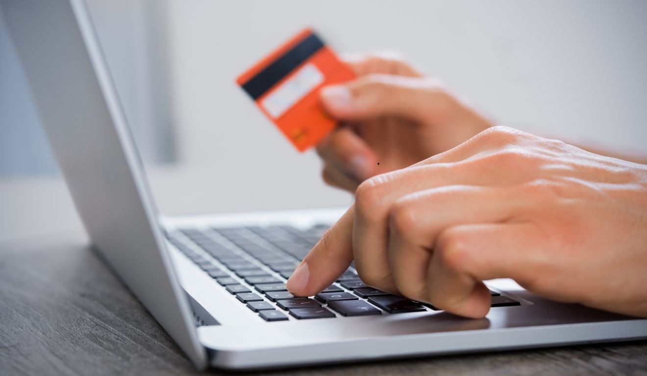 homem segurando cartão de crédito enquanto faz compra online