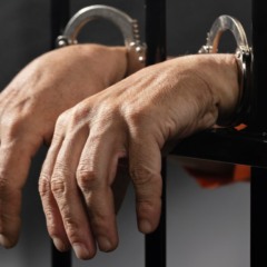 foto com imagem de mãos de um homem preso atrás das grades