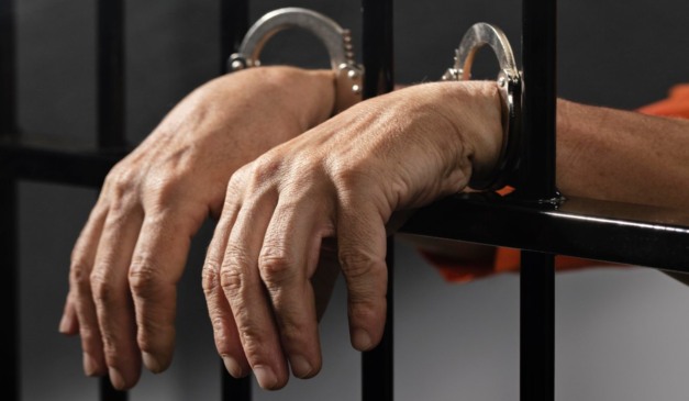 foto com imagem de mãos de um homem preso atrás das grades