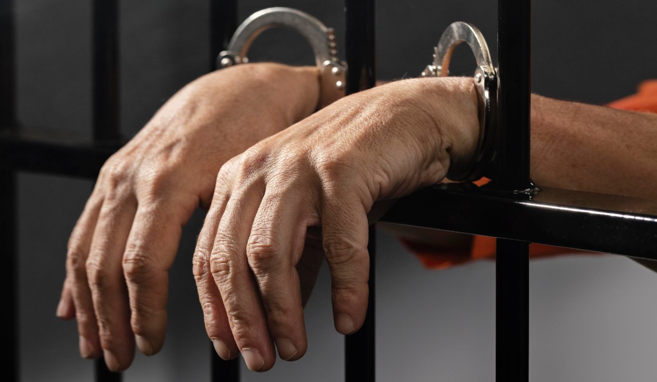 foto com imagem de mãos de um homem preso atrás das grades