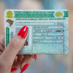 Paraná terá CNH gratuita para pessoas em vulnerabilidade social. Na imagem, vemos uma mão feminina, com as unhas pintadas de vermelho, segurando a Carteira de Habilitação Nacional.