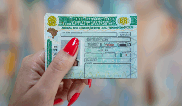 Paraná terá CNH gratuita para pessoas em vulnerabilidade social. Na imagem, vemos uma mão feminina, com as unhas pintadas de vermelho, segurando a Carteira de Habilitação Nacional.