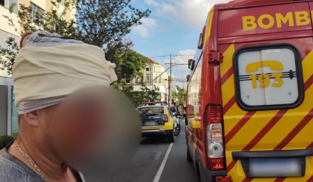 Um entregador foi agredido enquanto fazia uma entrega em Curitiba. Na imagem, vemos a vítima em primeiro plano, com o rosto borrado para garantir seu anonimato. Ao fundo, vemos uma ambulância do Siate.