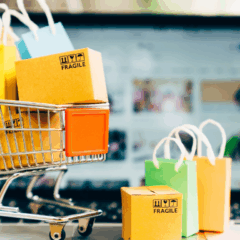 Descubra estratégias para vender mais na Black Friday 2025. Na imagem ilustrativa, vemos um carrinho de supermercado pequeno, com pacotes de compra. Ao fundo, vemos um notebook, desfocado.