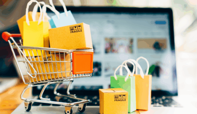 Descubra estratégias para vender mais na Black Friday 2025. Na imagem ilustrativa, vemos um carrinho de supermercado pequeno, com pacotes de compra. Ao fundo, vemos um notebook, desfocado.