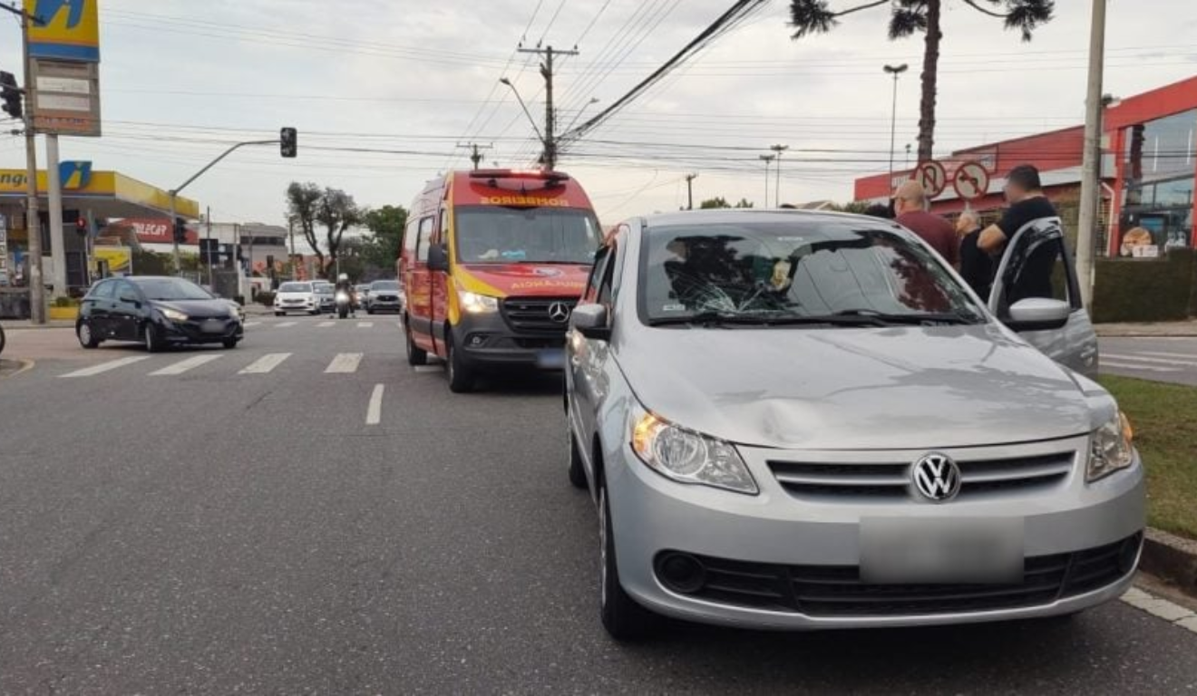 Estudantes foram atropeladas enquanto estavam mexendo celular. Na imagem, vemos o carro do acidente com o capô amassado, com uma ambulância do Corpo de Bombeiros logo atrás.