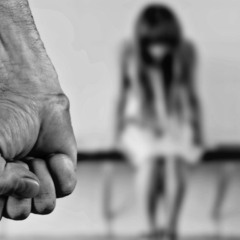 Homem abusa de adolescente em sua casa. Na imagem ilustrativa, em preto e branco, vemos um punho fechado em primeiro plano. Ao fundo, vemos uma garota, cabisbaixa, sentada em um banco.