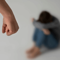 Homem ameaça de morte sua ex-companheira. Na iamgem ilustrativa, vemos uma mão branca em primeiro plano. Ao fundo, há uma mulher desfocada, ela está sentada, com os braços sobre os joelhos, escondendo o rosto nos braços.