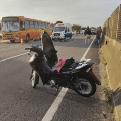 Jovem sofre acidente com motocicleta na BR-277, em Curitiba. Na imagem, vemos a motocicleta parada na rodovia, com uma ambulância e um ônibus ao fundo.