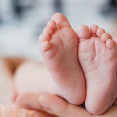 Pé de bebê e pessoa encostando com a mão nele