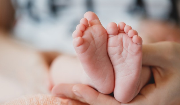 Pé de bebê e pessoa encostando com a mão nele