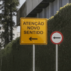 Quatro ruas de Curitiba terão alteração de sentido a partir do dia 14 de novembro. Na imagem, vemos uma placa amarela com o texto "Atenção Novo Sentido", indicando o sentido único de circulação de uma rua.