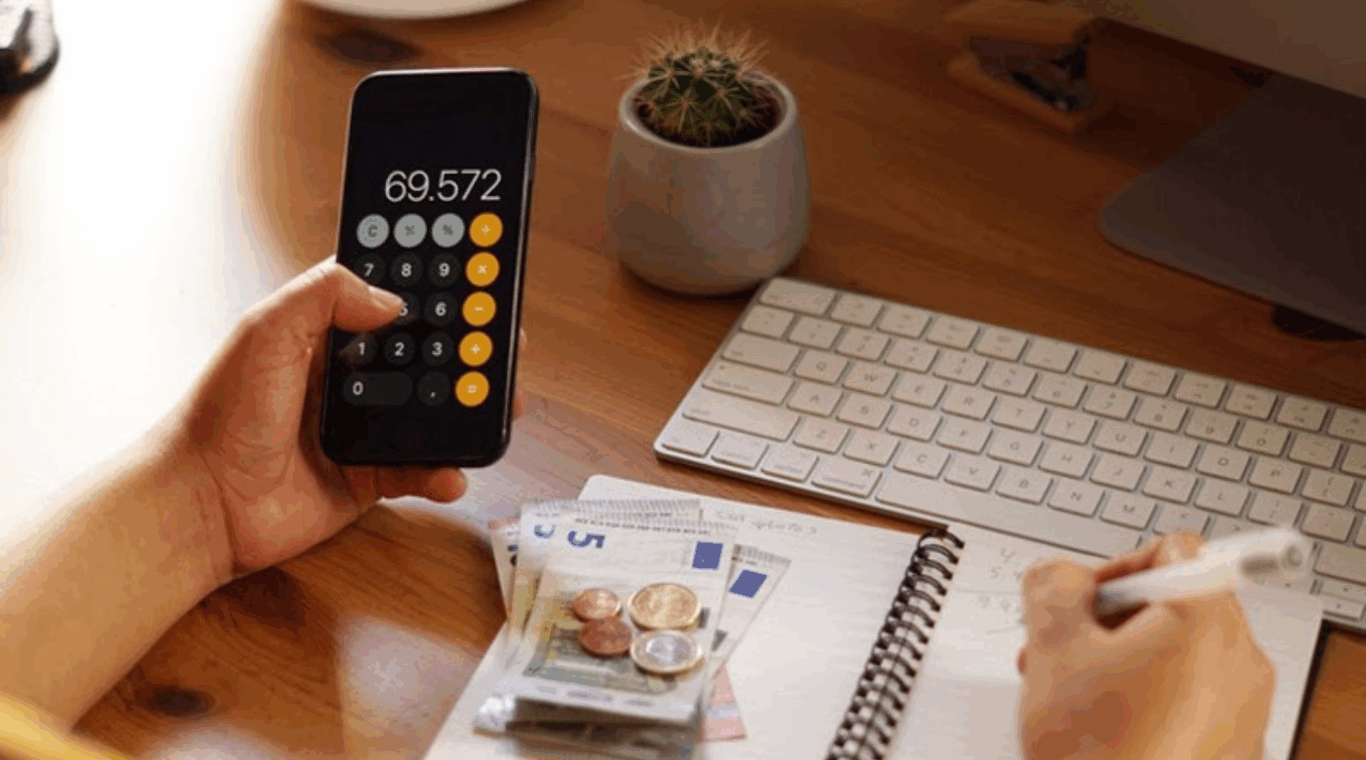 pessoa calculando impostos no celular, com dinheiro na mesa