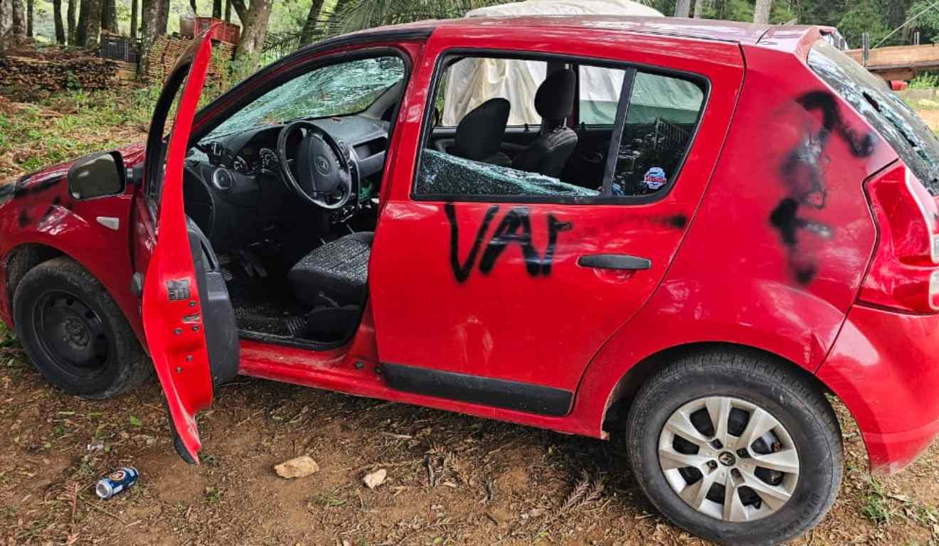 Sandero vermelho com pichação e vidros quebrados